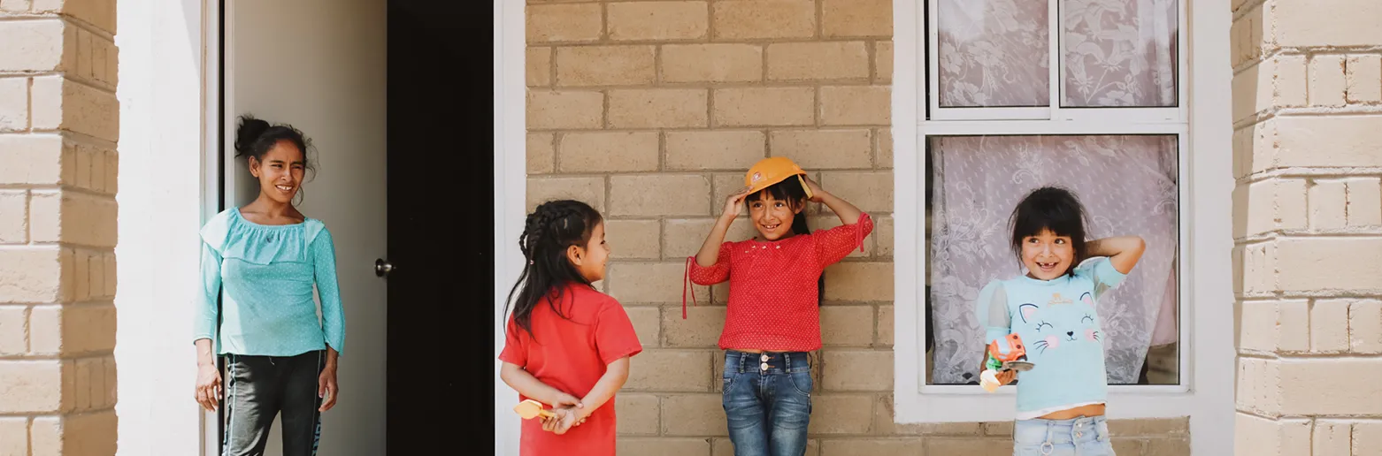Four individuals standing on their front porch, holding toys and smiling