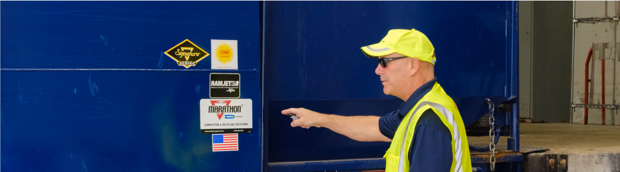 Worker inspecting a large blue commercial trash compactor