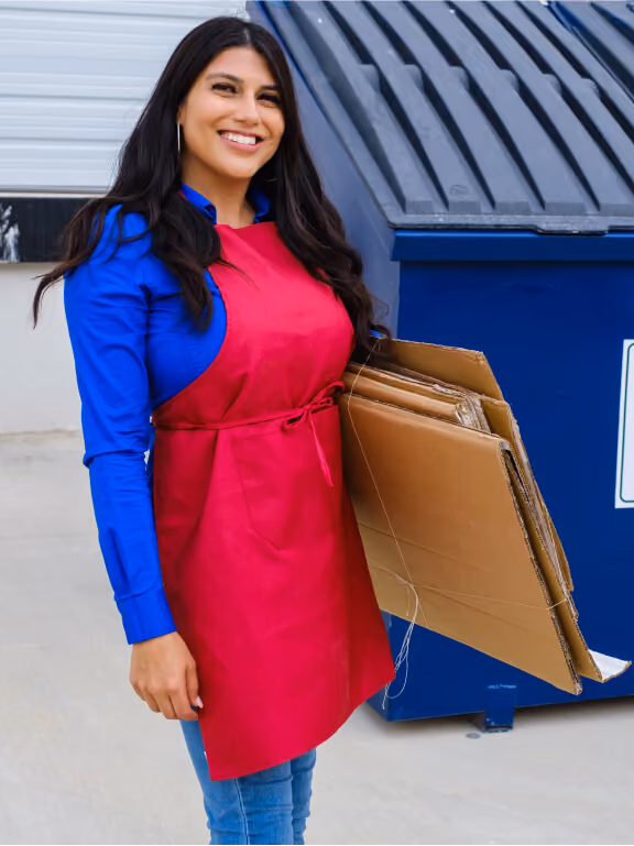 Woman carrying flattened cardboard to a commercial recycling dumpster