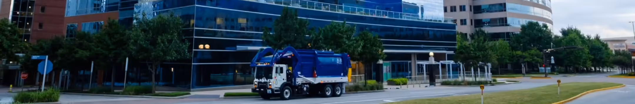 Blue garbage truck driving past an office building