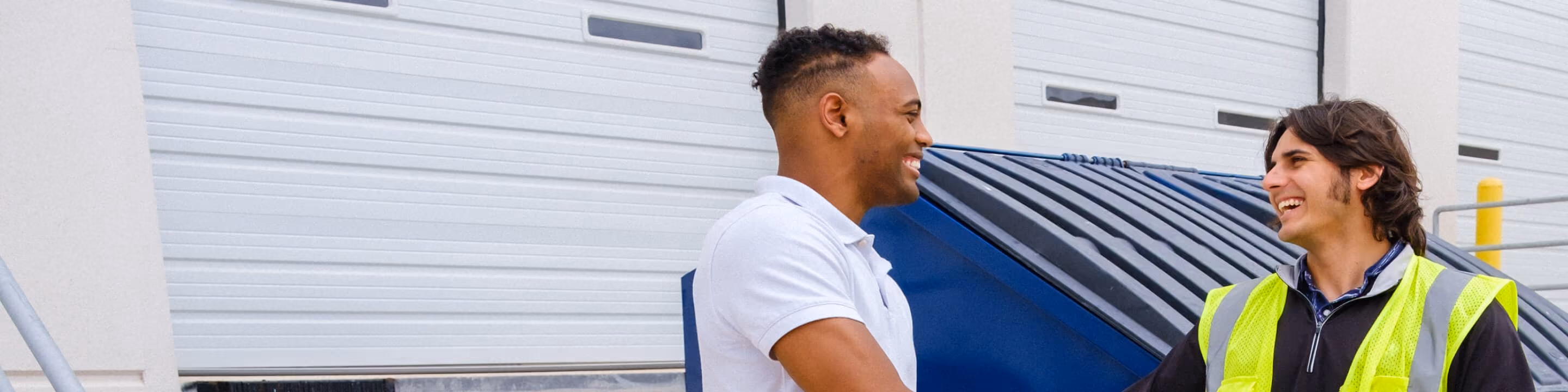 Two workers talking beside a blue dumpster at a loading dock