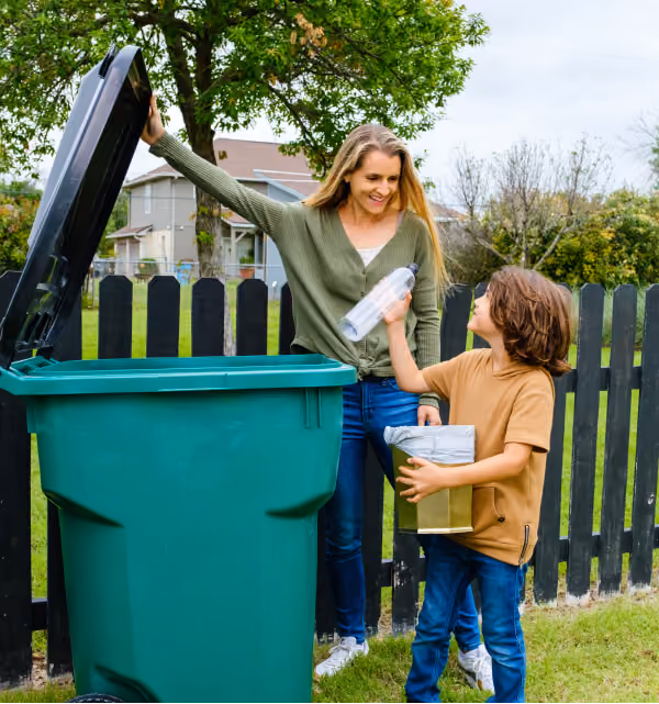 Woman and boy placing recyclables in a green curbside bin