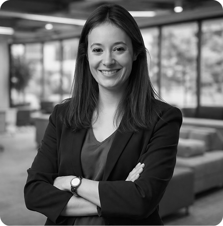 Smiling woman with long hair wearing a blazer and watch, standing with arms crossed in a modern office lounge.