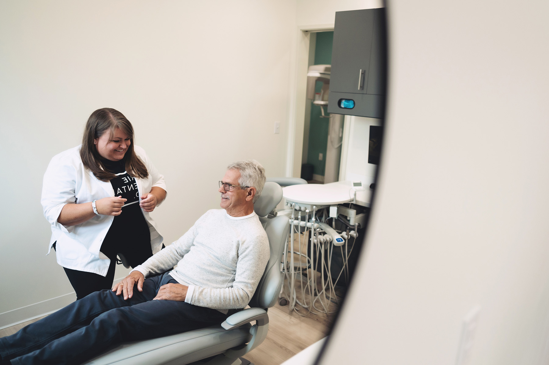 Male patient in dental chair smiling at female dentist in white coat in a dental office.