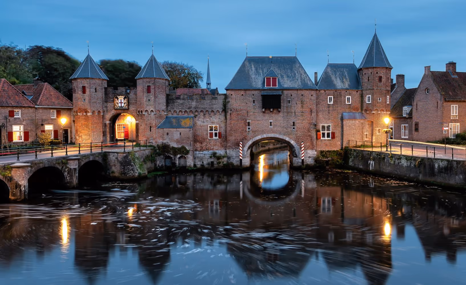 Middeleeuwse stadspoort en gracht met weerspiegeling in Leusden tijdens de avondschemering.