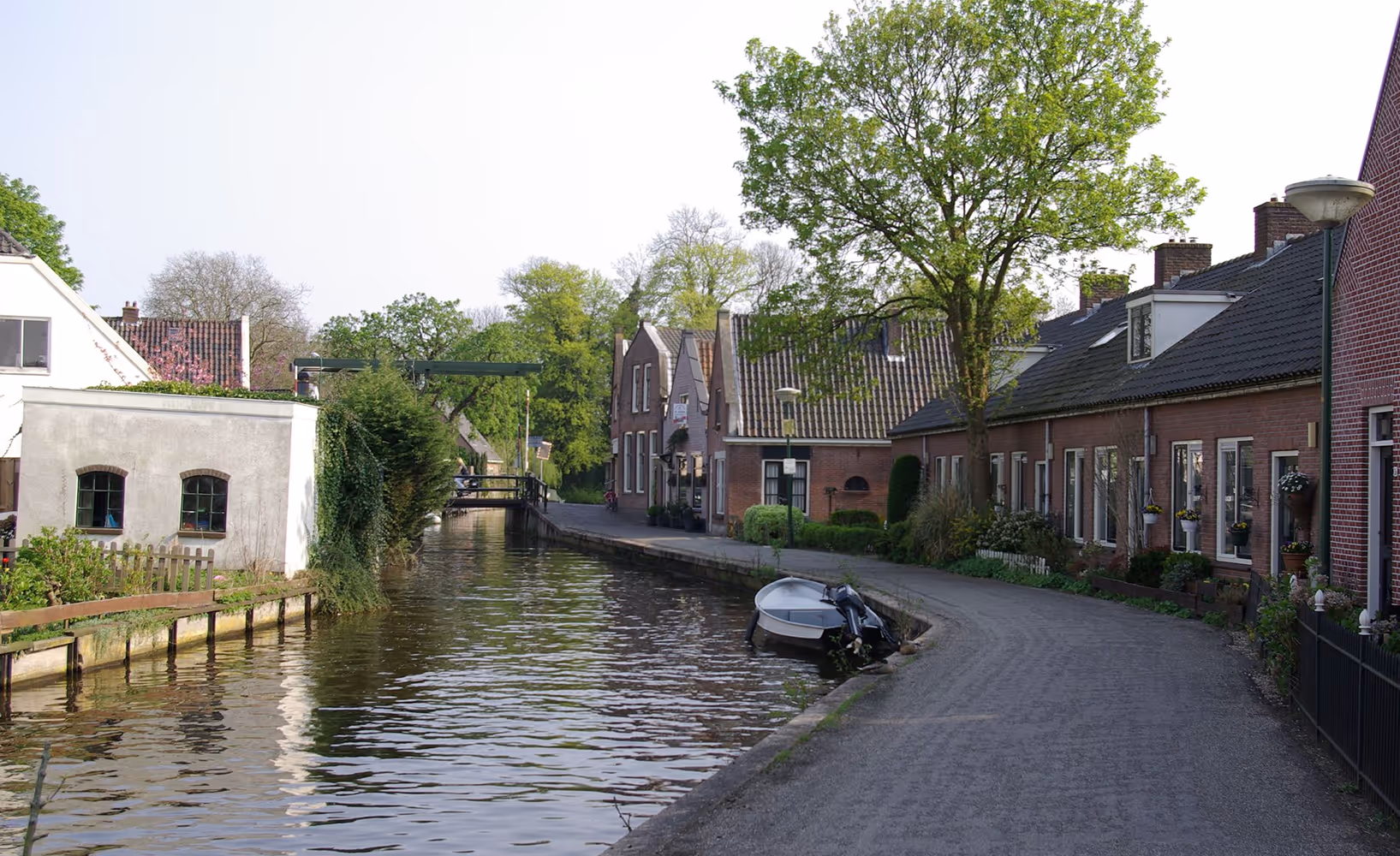 Smalle gracht met woonhuizen, bomen en een kleine boot in een rustig dorp aan het water in Abcoude.