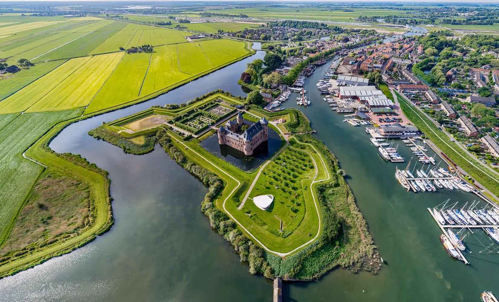 Luchtfoto van Muiderslot met omliggende vesting, water en haven in Muiden.