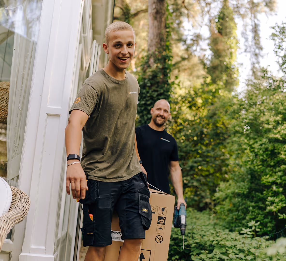 Monteurs van Elite Klimaat Groep dragen apparatuur voor een installatie bij een woning in een groene omgeving.