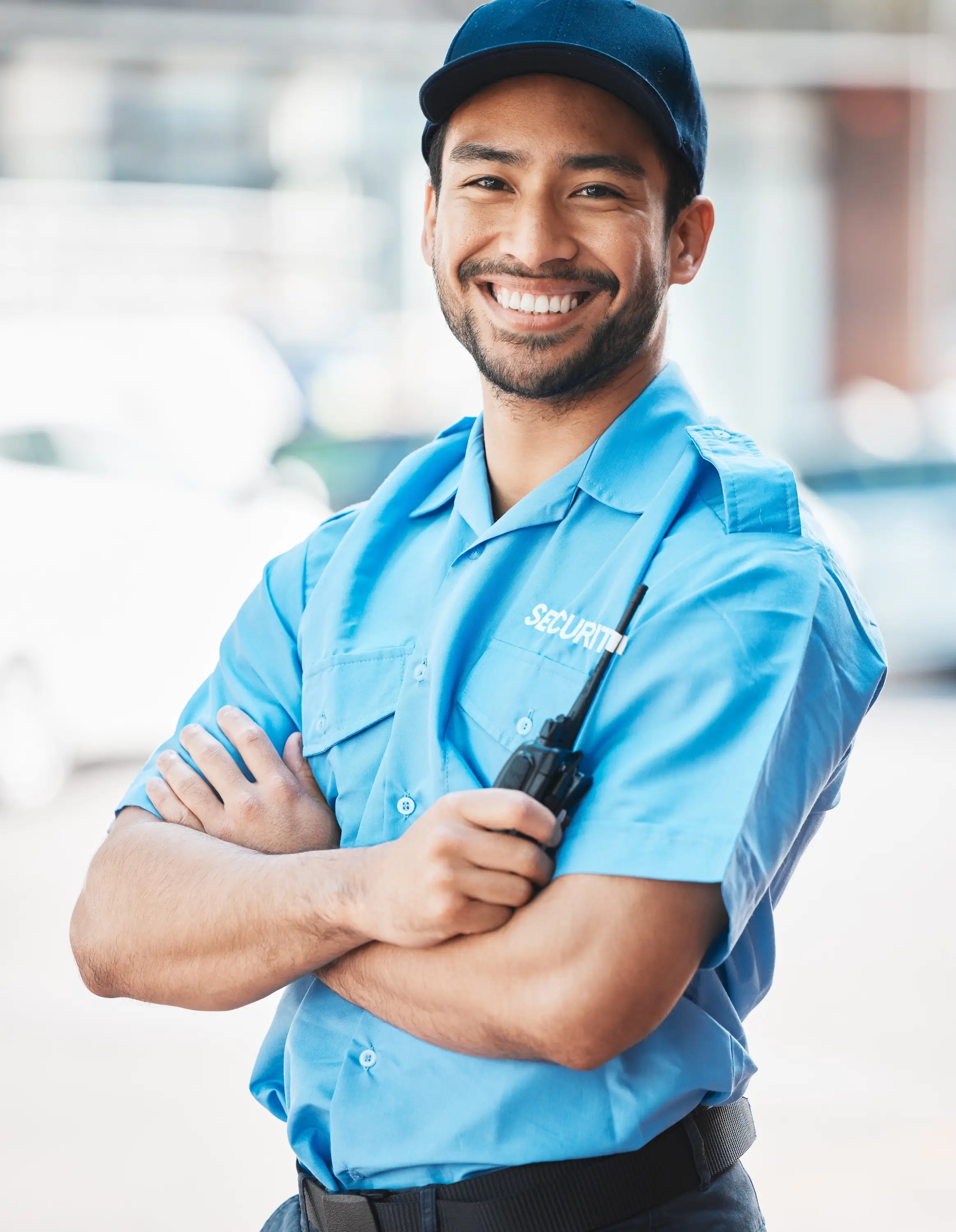 A smiling security guard wearing a blue shirt and hat stands confidently.