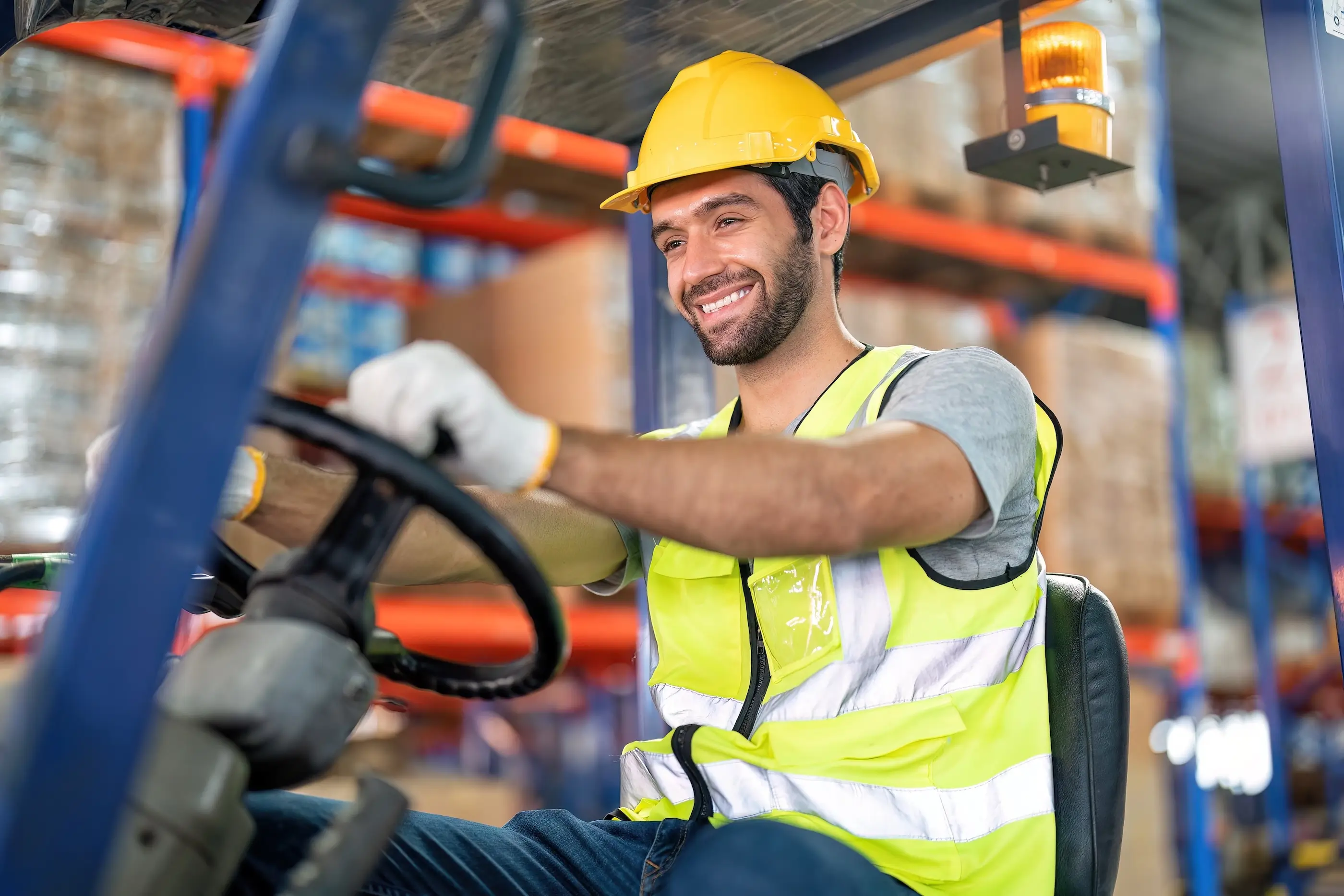 A smiling man wearing a safety vest operates a forklift, showcasing a positive work environment.