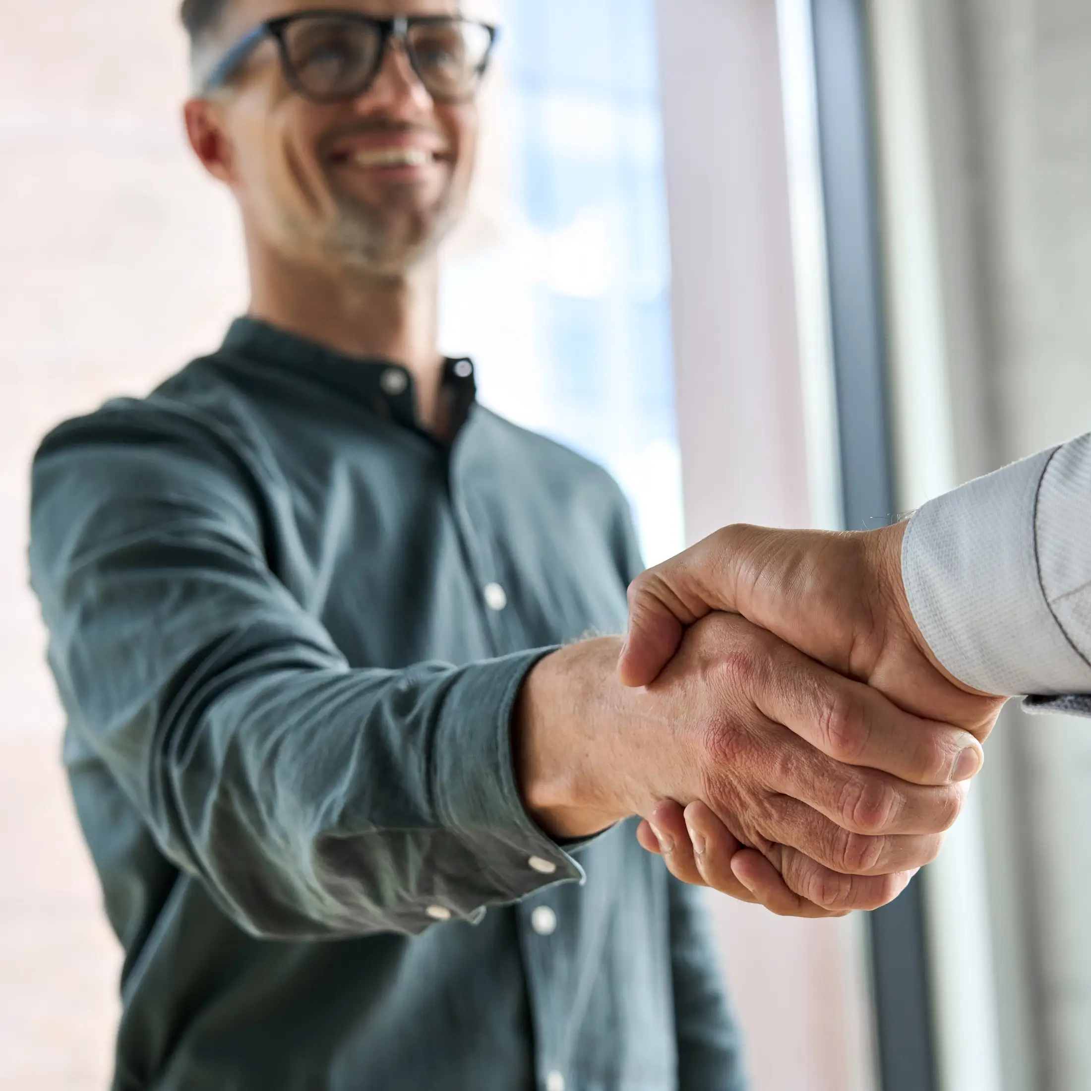 Two men shaking hands in a modern office setting, symbolizing a business agreement or partnership.