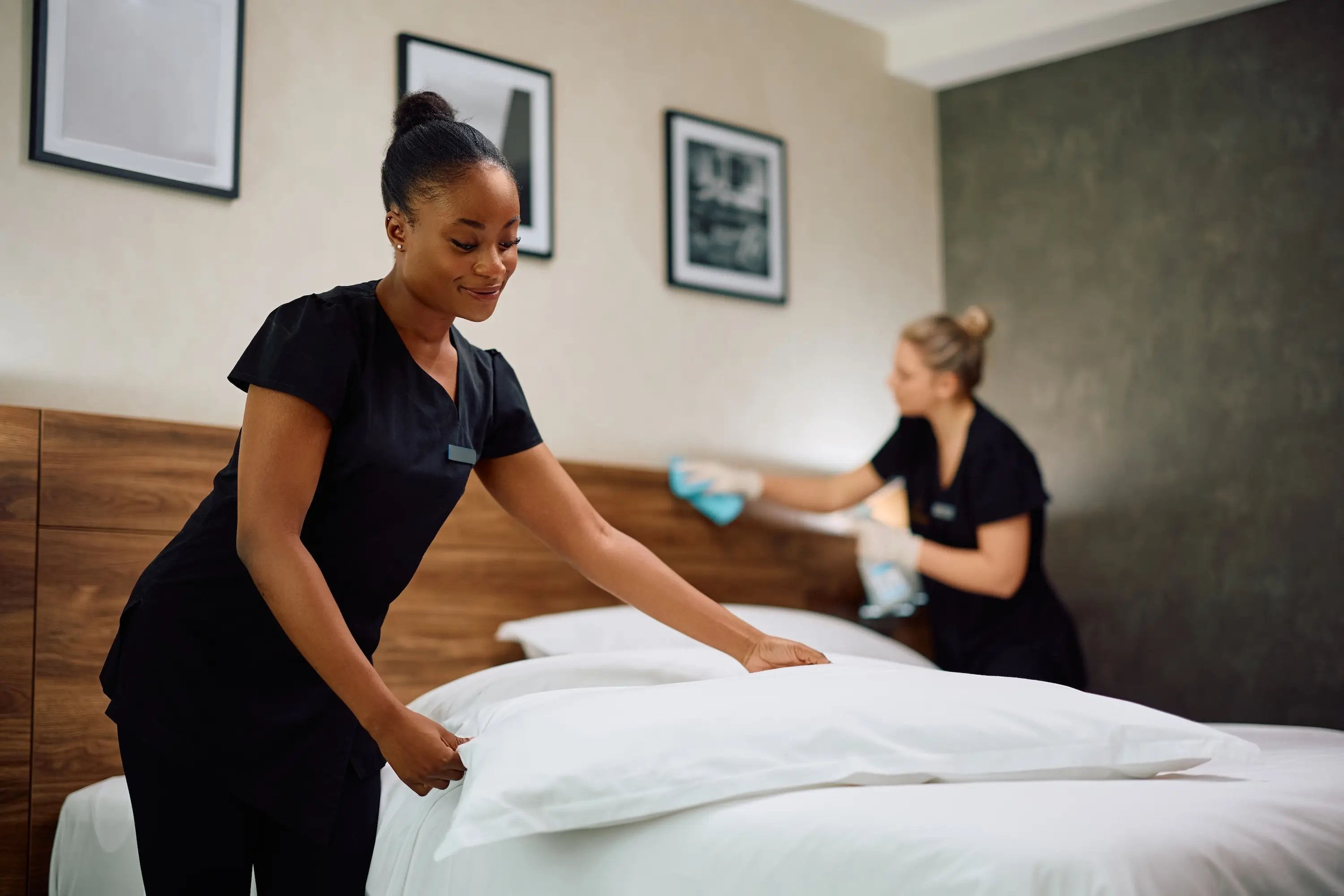 Two women in black shirts are cleaning a bed, focusing on making it tidy and presentable.