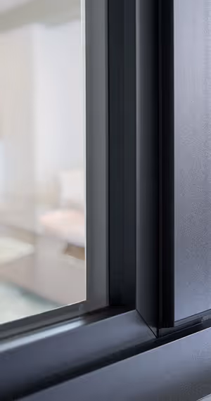 Close-up of a dark gray window frame with a blurred interior room visible through the glass.