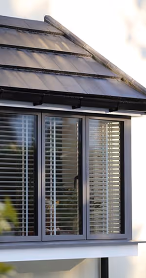 Close-up of a modern house window with closed horizontal blinds and a dark roof above it.