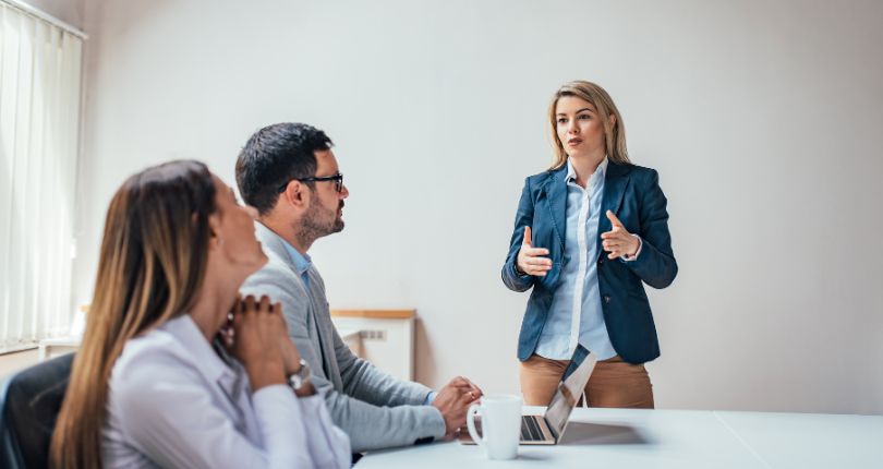 Deux apprenants assis à une table en train de suivre une formation d'anglais avec une formatrice qui s'adresse à eux - Monceau Langues