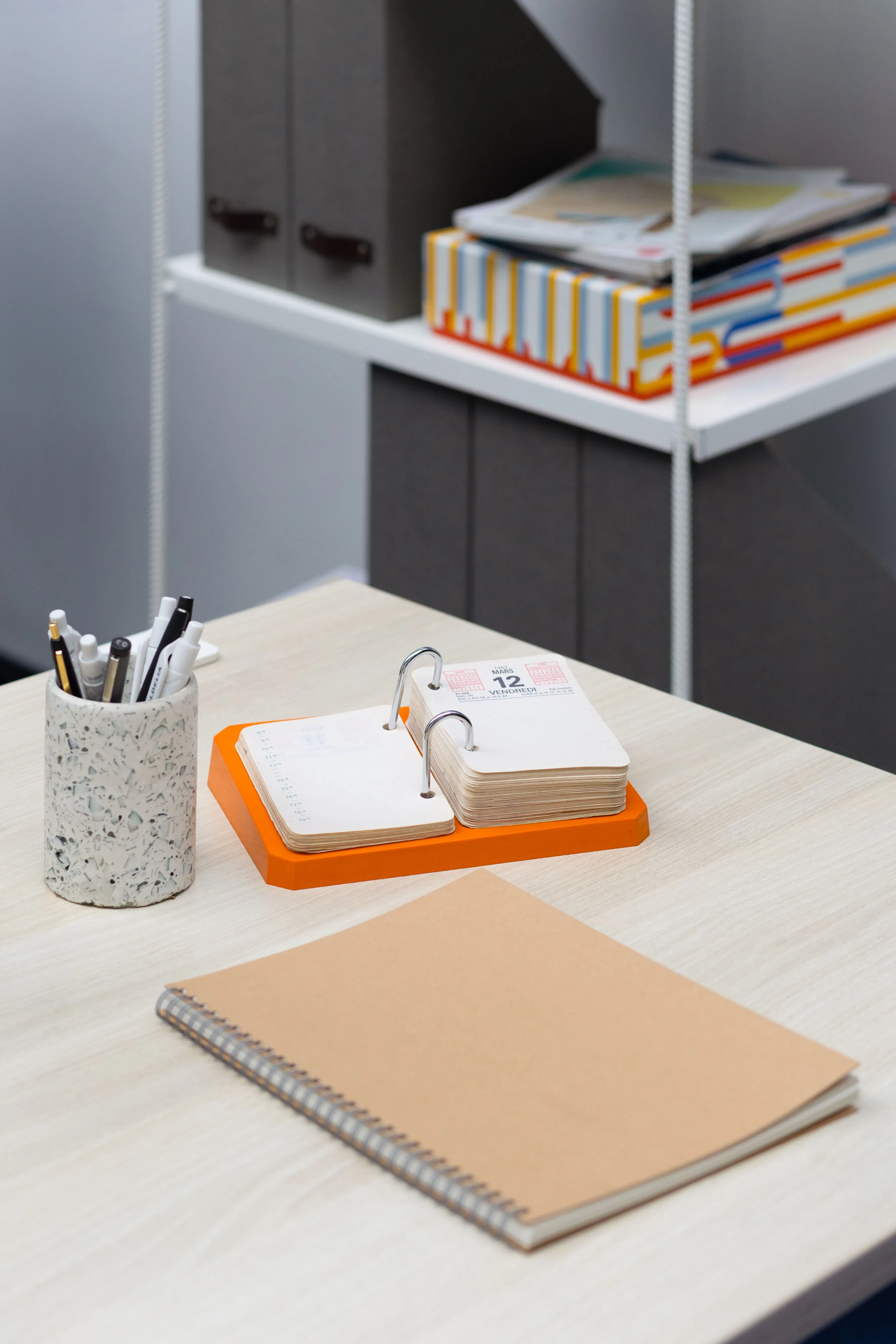 Détail d'un poste de travail : pot à crayons en terrazzo et carnet posés sur le bureau