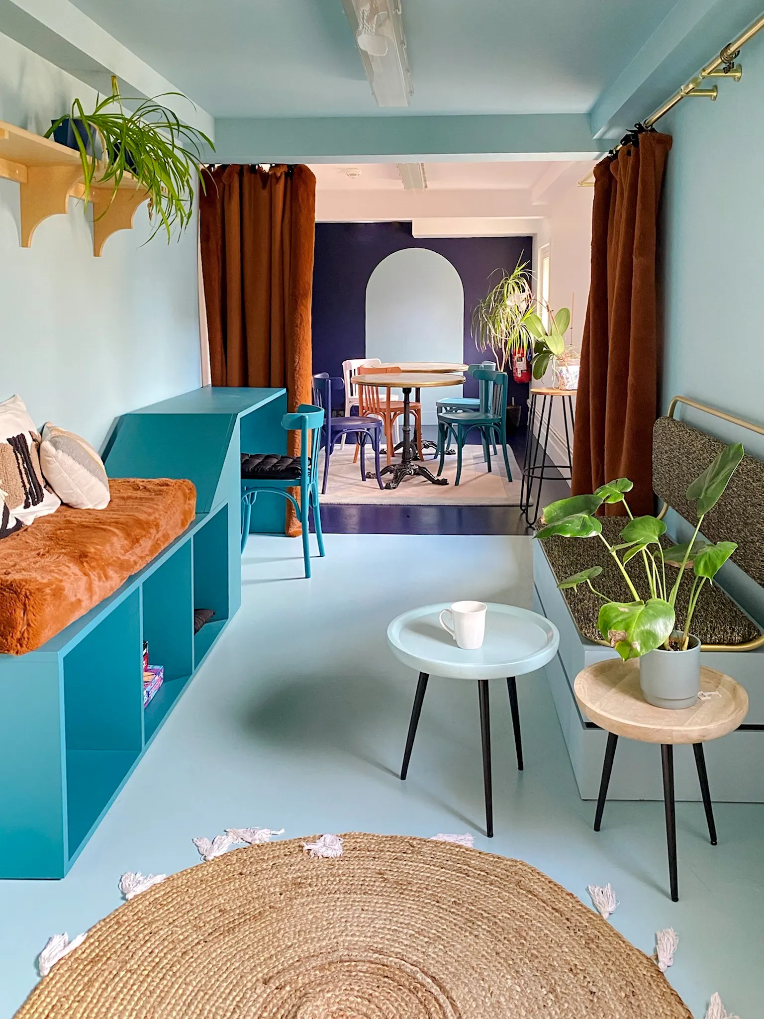Espace hybride coloré avec banquette orange, bar bleu et tables rondes
