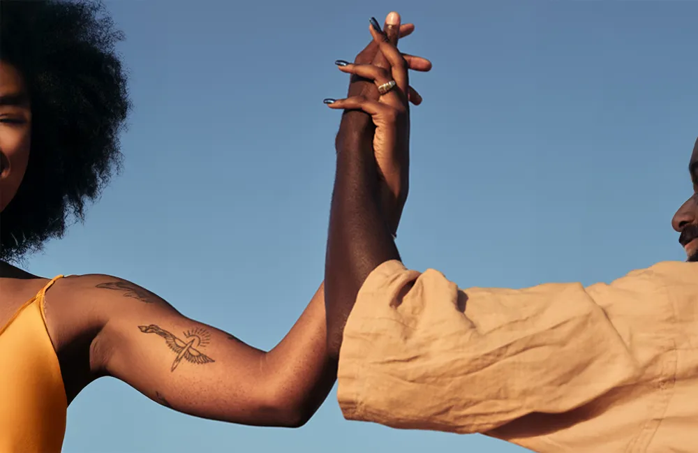 Two people reaching up to clasp hands against a clear blue sky