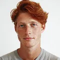 Portrait of a young man with fair skin, red hair, and light blue eyes, wearing a gray shirt against a plain white background.