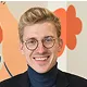 Person with short light hair, wearing round glasses and a dark turtleneck, smiling in front of a white background with orange shapes.