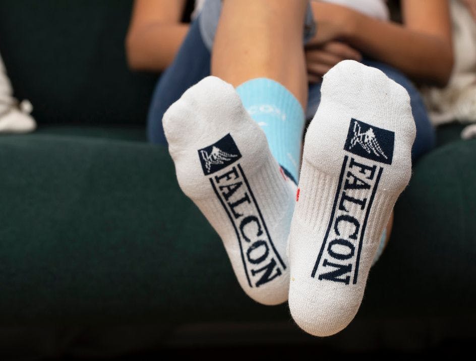 Custom knitted athletic socks for Falcon with the logo knitted into the sole of the sock being worn by a woman sitting on a green couch