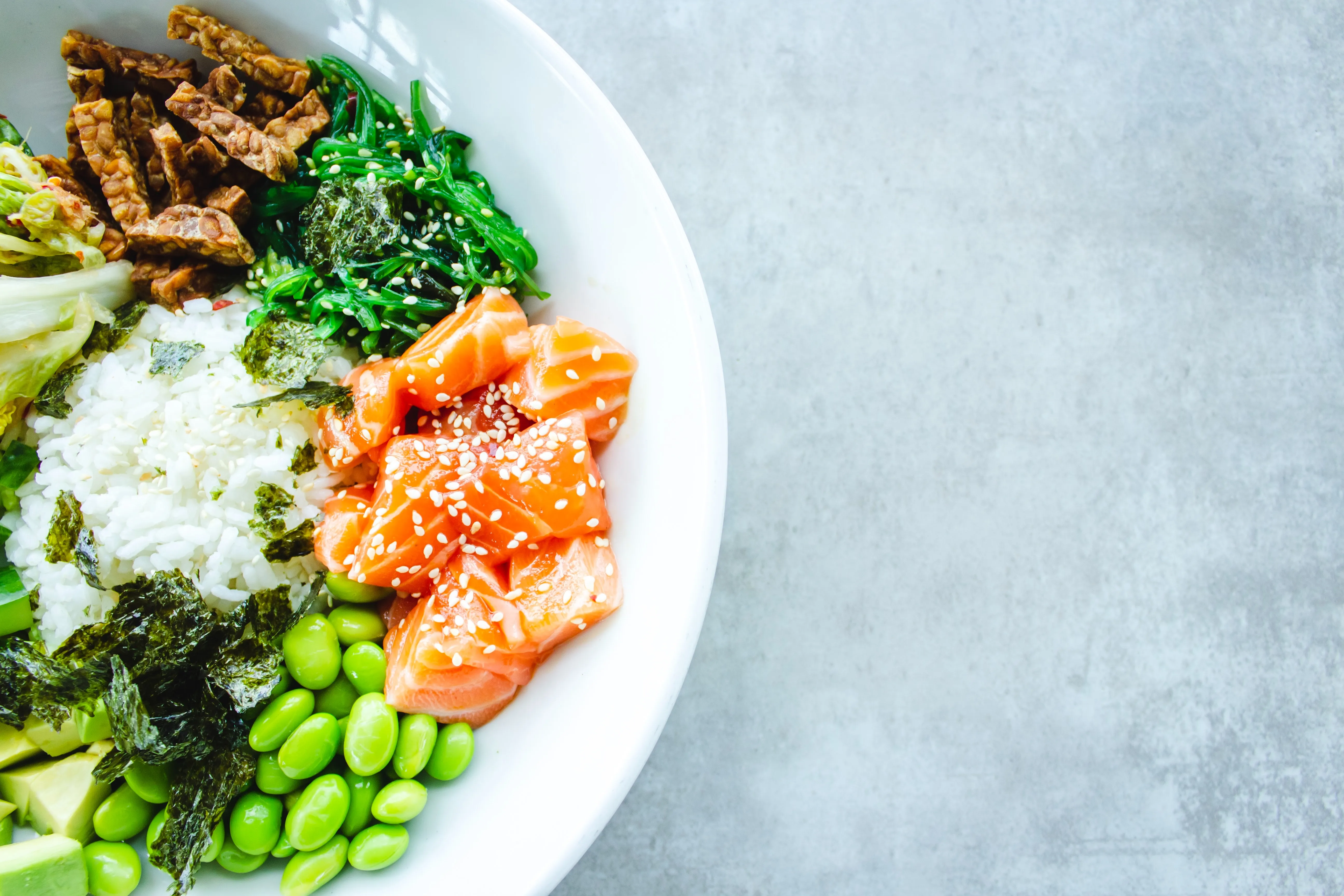 A bowl of brightly colored healthy vegetables, rice, and salmon.
