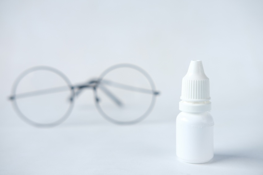 Bottle of lubricating eye drops beside a pair of glasses