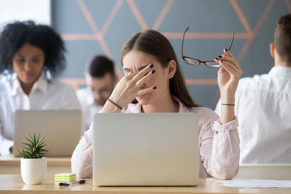 Person rubbing tired, irritated eyes while using a laptop at work