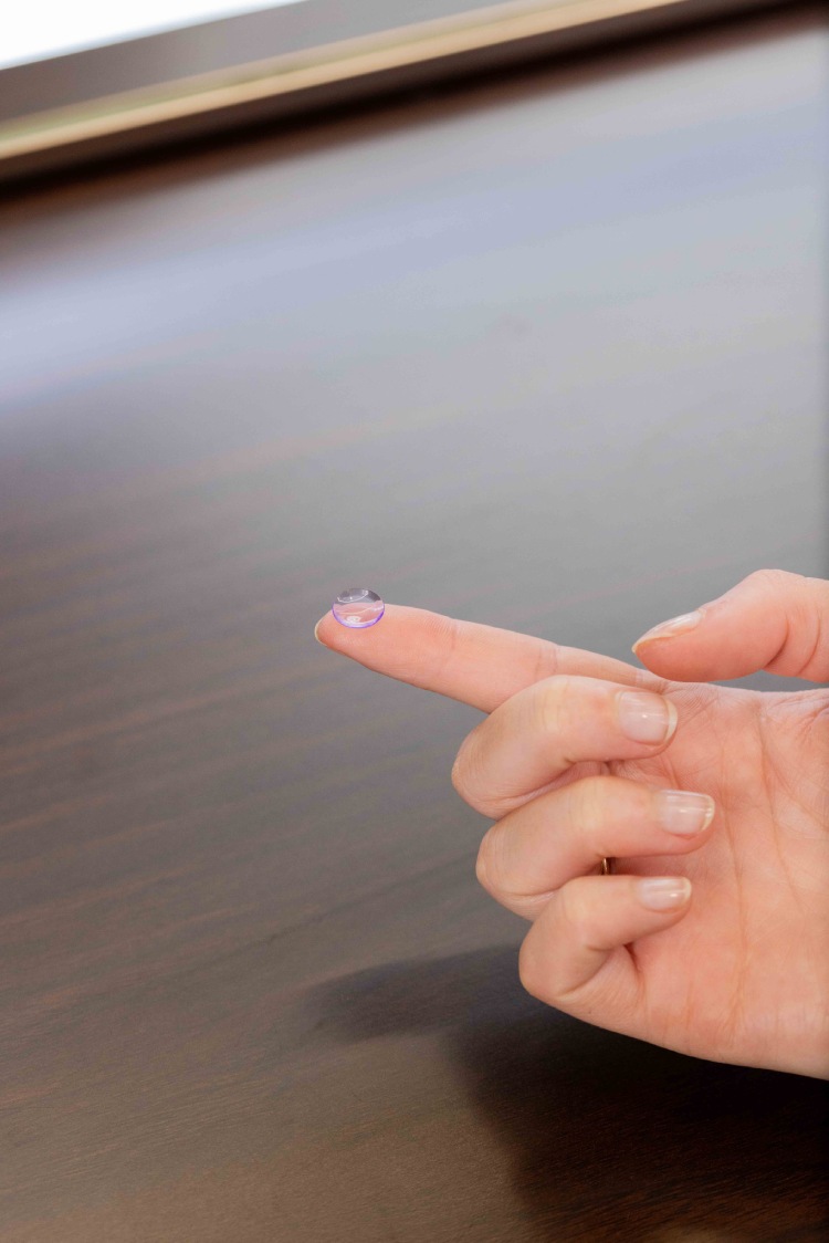 Orthokeratology night lens balanced on a fingertip before insertion