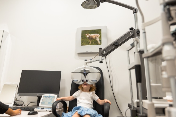 Young child completing a vision test with a phoropter while viewing a picture target