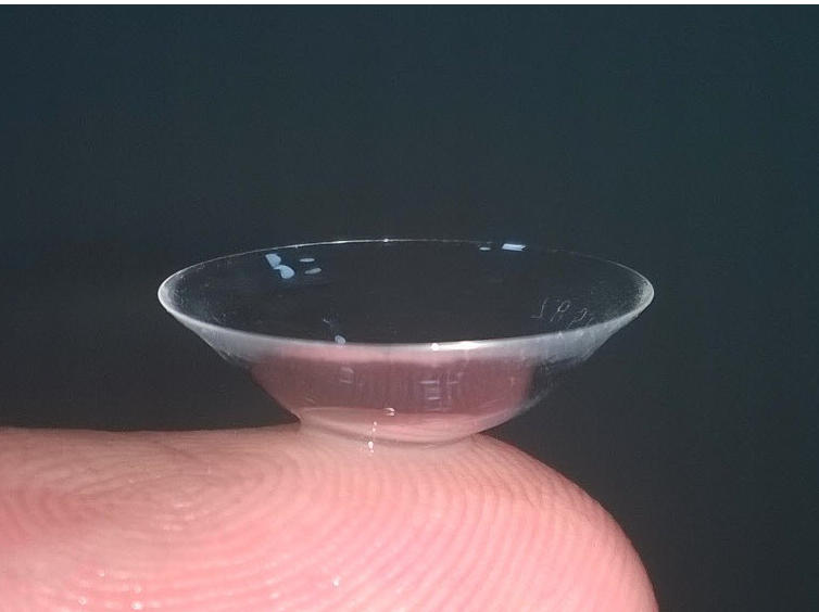 Close-up of a scleral contact lens balanced on a fingertip