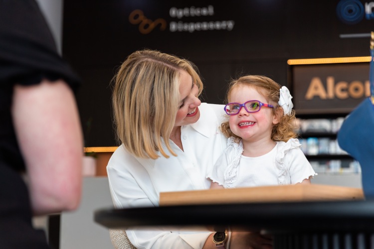 Young child wearing new glasses with her parent after an eye test