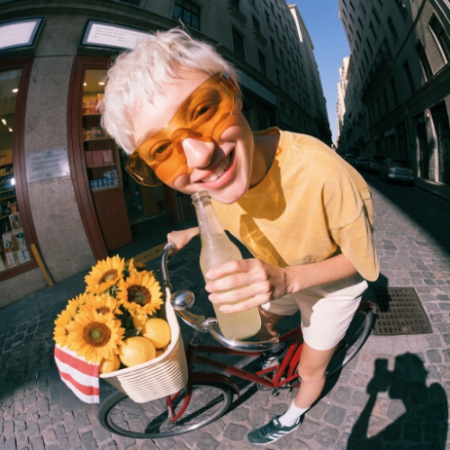 Fisheye photo of a smiling person in orange sunglasses on a bicycle with sunflowers, made with Recraft