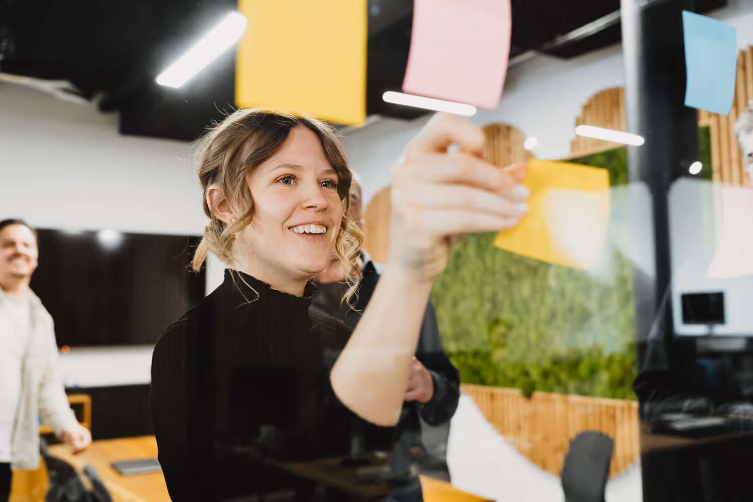 I*AM Mitarbeiterin klebt Post-its an die Wand und lacht