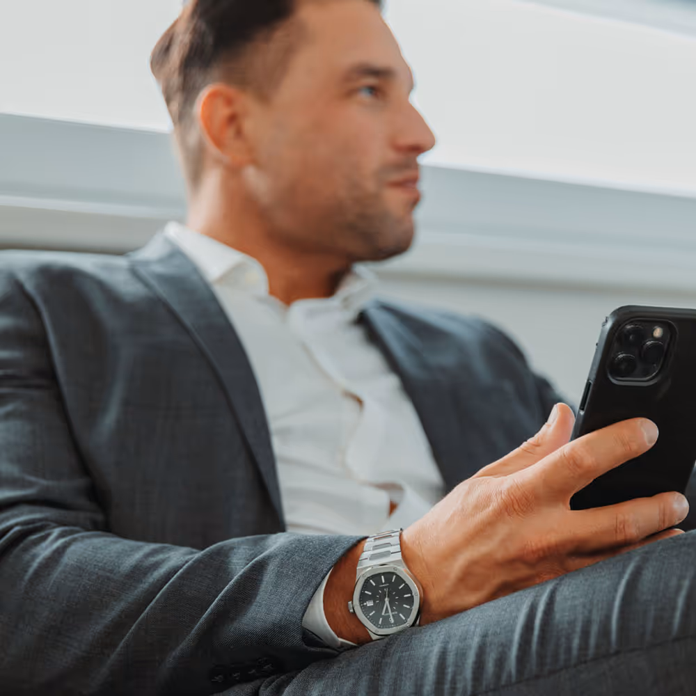 Business-Mann mit Rosenbusch-Uhr am Handgelenk und Smartphone in der Hand – Sinnbild für Stil und Fokus.