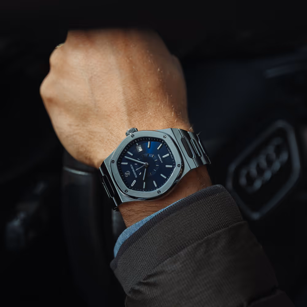 Rosenbusch-Uhr mit blauem Zifferblatt am Handgelenk eines Autofahrers – Eleganz und Präzision im Alltag.