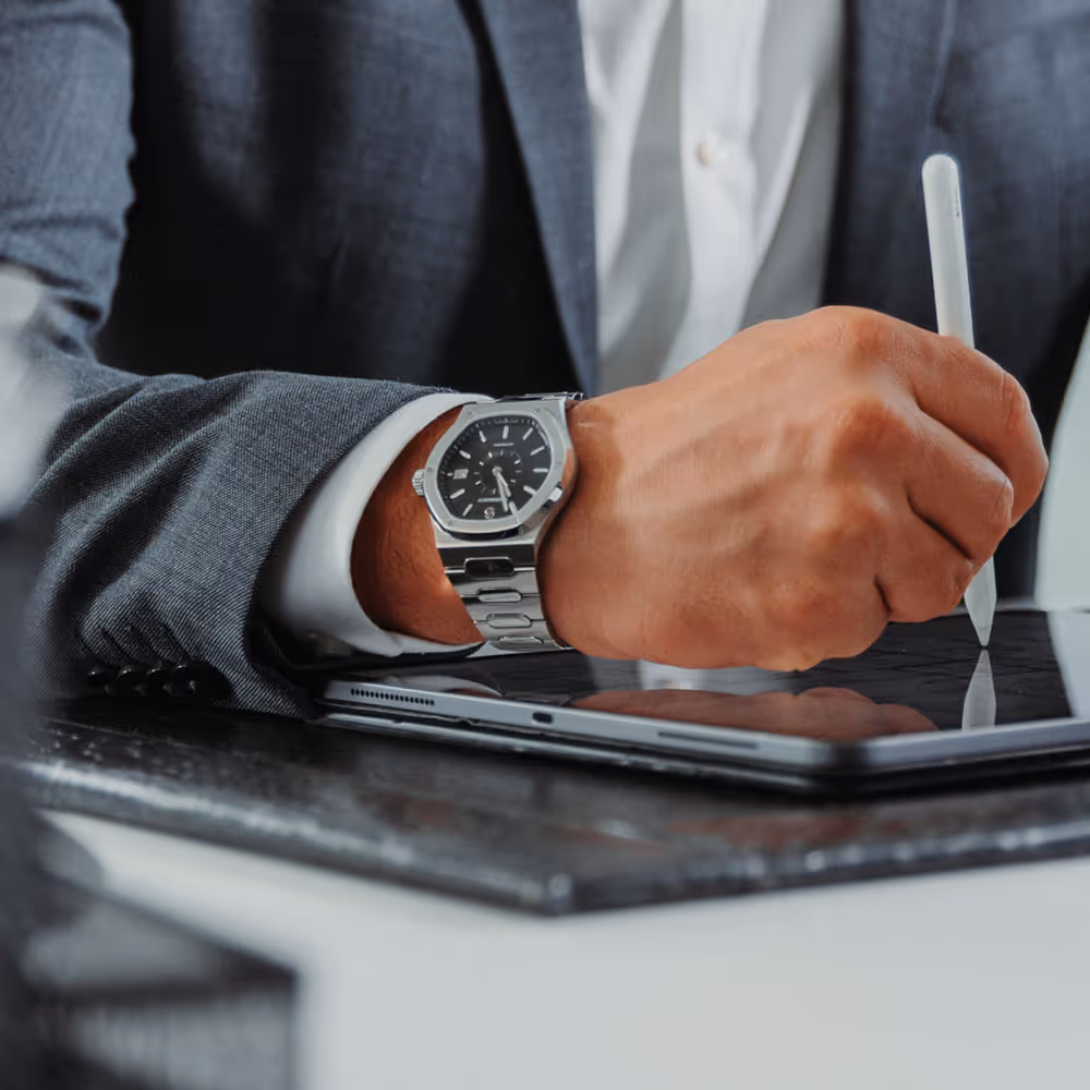 Close-up eines Handgelenks mit Rosenbusch-Uhr bei der Arbeit mit einem Tablet – Eleganz trifft Produktivität.