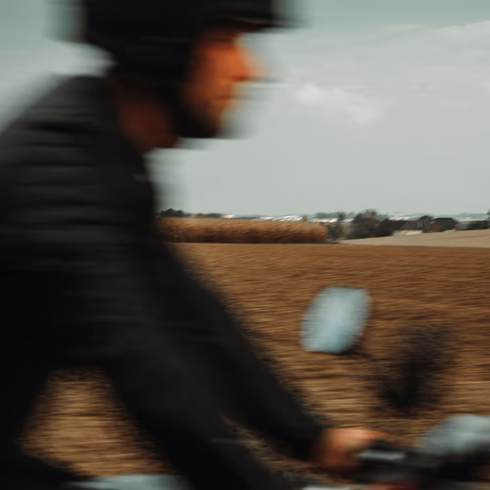 Bewegungsunschärfe eines Motorradfahrers vor offenem Feld – Gefühl von Geschwindigkeit und Freiheit.