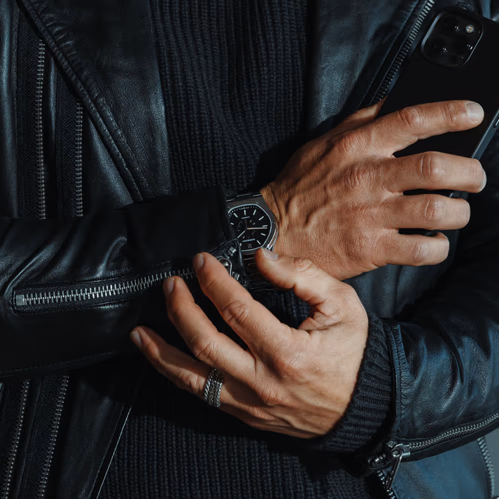 Close-up einer Hand mit Rosenbusch-Uhr beim Anpassen des Lederärmels – maskulin, urban, detailverliebt.