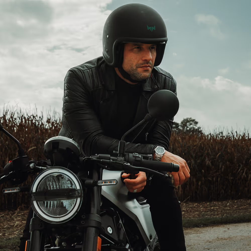 Motorradfahrer mit Helm und Rosenbusch-Uhr an einer Landstraße – Abenteuer trifft auf Präzision.