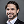 Smiling man with dark hair and beard wearing a white shirt and black blazer against a gray background.