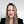 Smiling woman with long blonde hair wearing a black blazer against a plain light background.