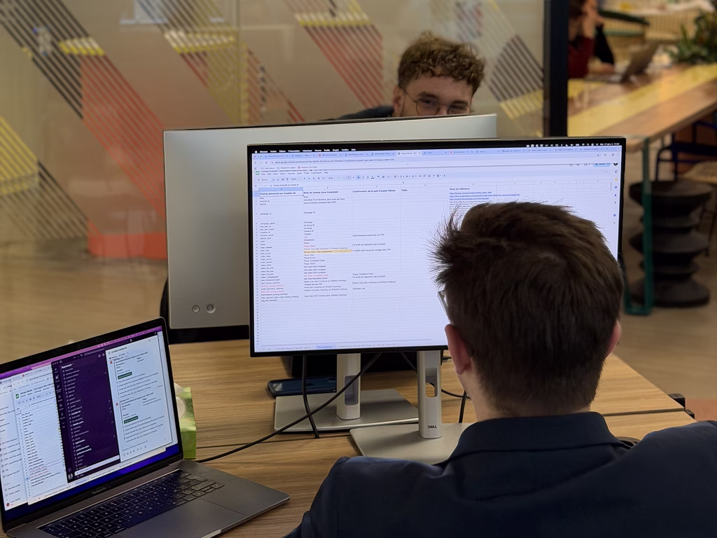 Deux personnes travaillant sur des ordinateurs dans un bureau moderne avec écran et ordinateur portable.