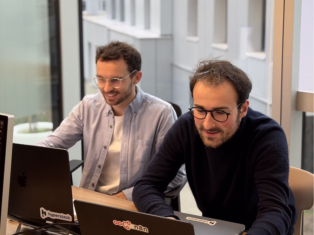 Deux hommes travaillant ensemble sur des ordinateurs portables en face d'une grande fenêtre en bureau.