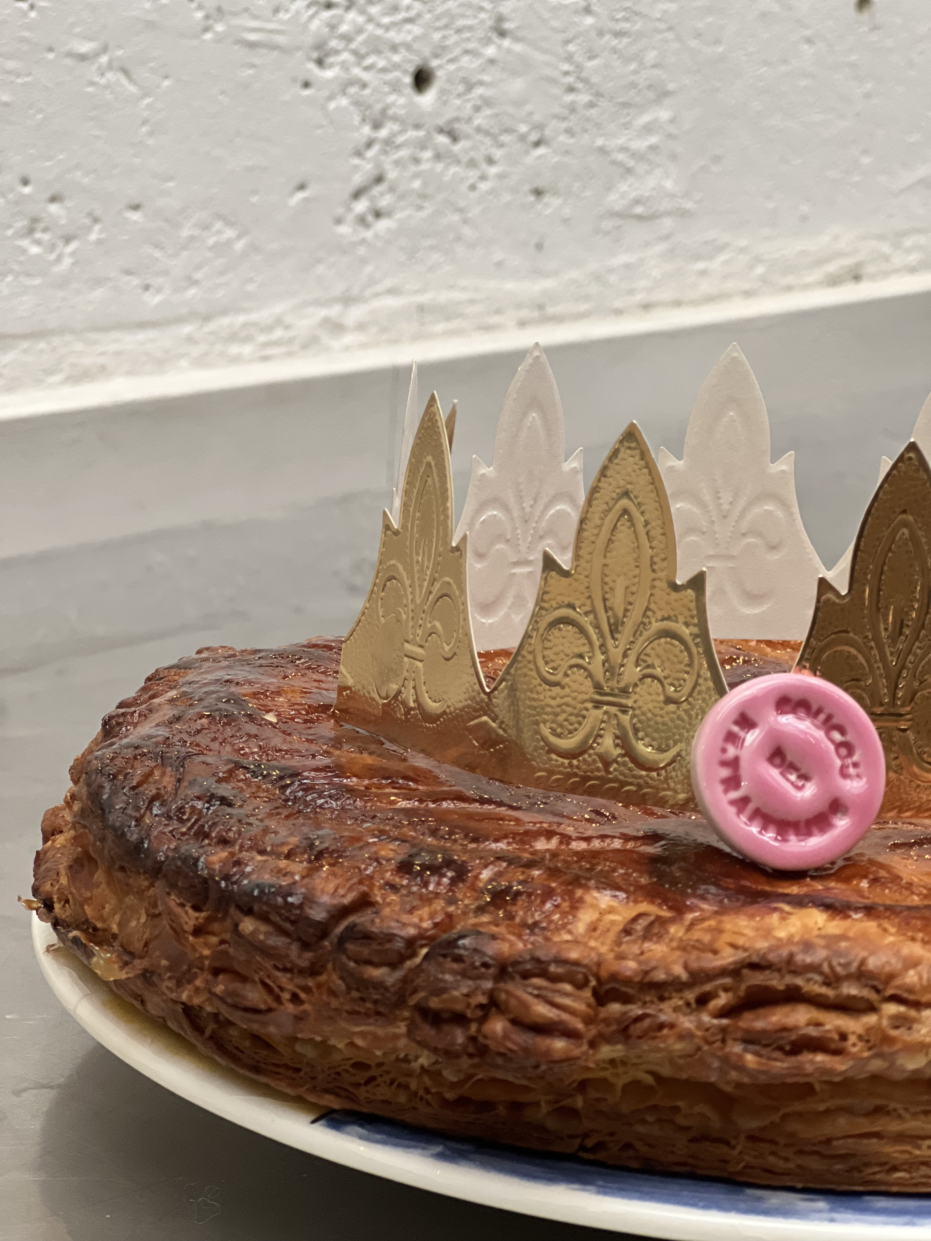 Gros plan sur un gâteau feuilleté doré recouvert d'une couronne décorative en papier doré et d'une fève en plastique rose.