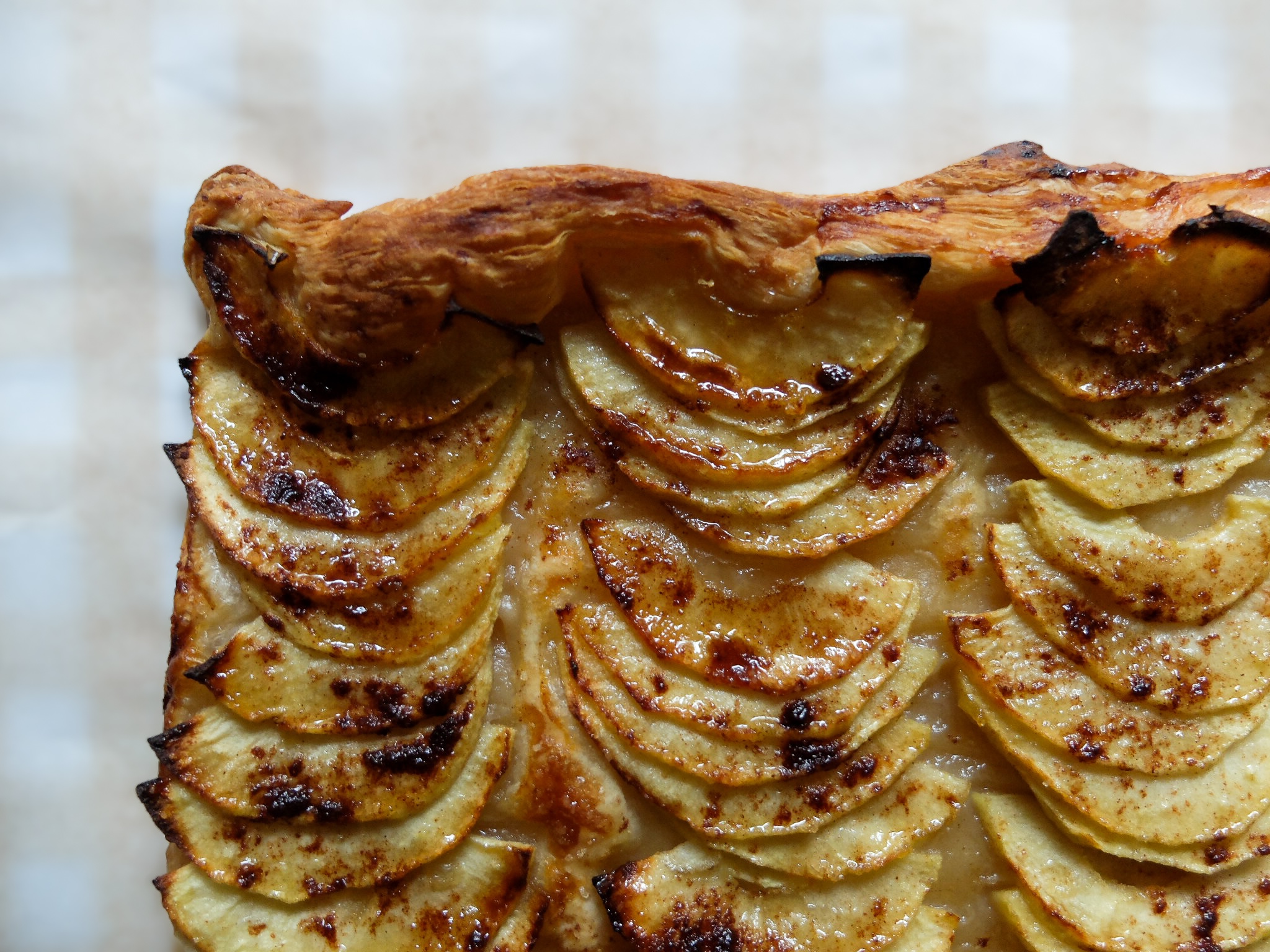 Close-up of a baked apple tart with golden-brown puff pastry and thinly sliced, caramelized apple pieces arranged in rows.