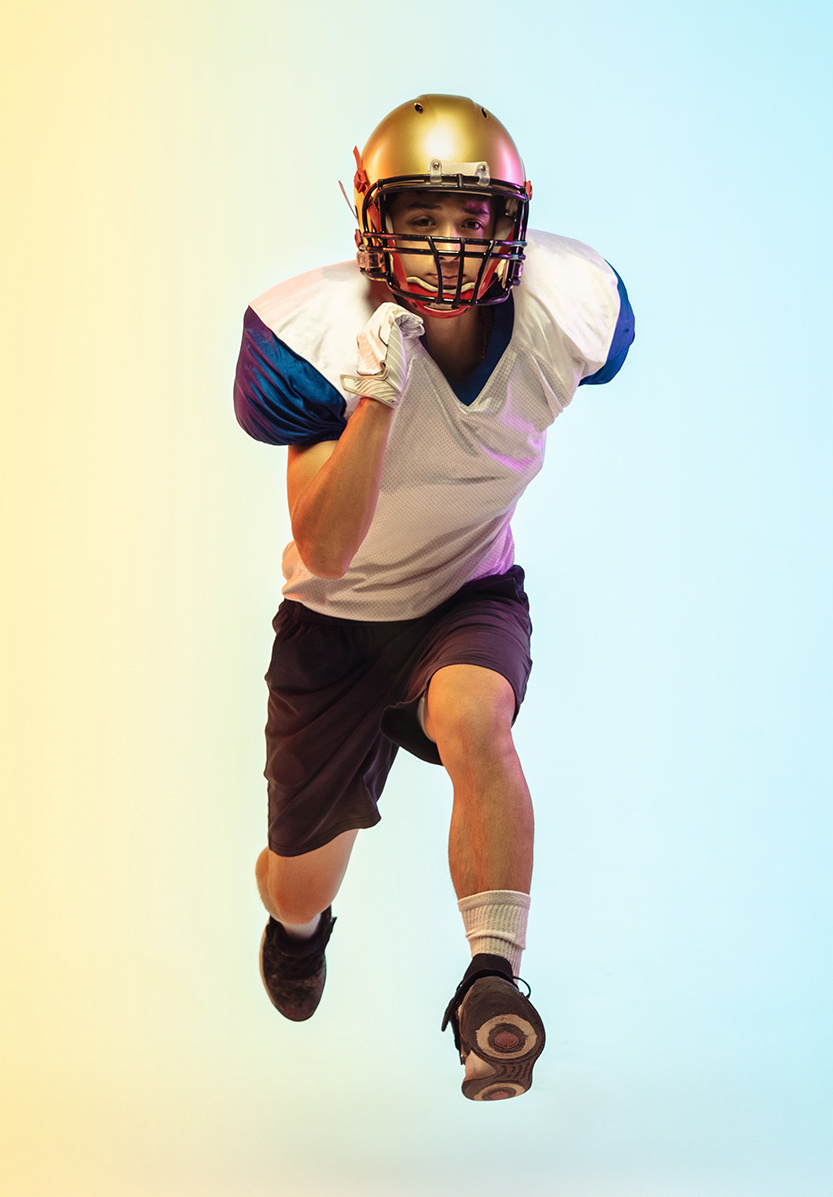 A boy in a football uniform running at the camera against a light background
