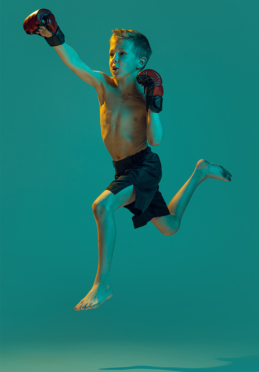 A young boy with boxing gloves jumping in the air against a teal background