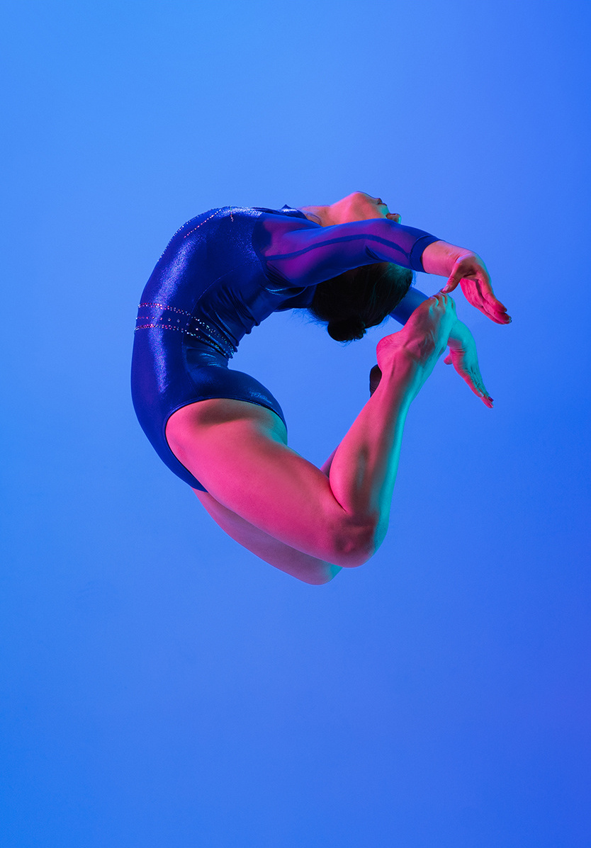 A female gymnast performing a sheep jump against a blue background