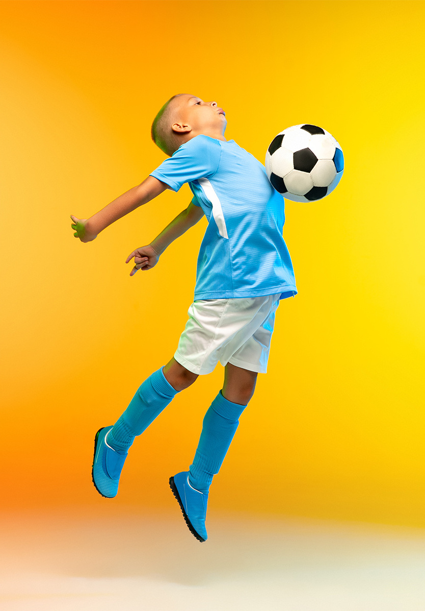 A young boy hitting a soccer ball with his chest mid-air against a yellow background
